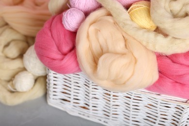 Photo of Soft felting wool and yarns in wicker basket on grey table, closeup