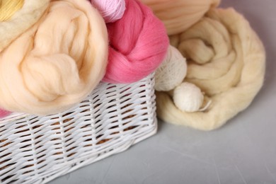 Photo of Soft felting wool and yarns in wicker basket on grey table, closeup