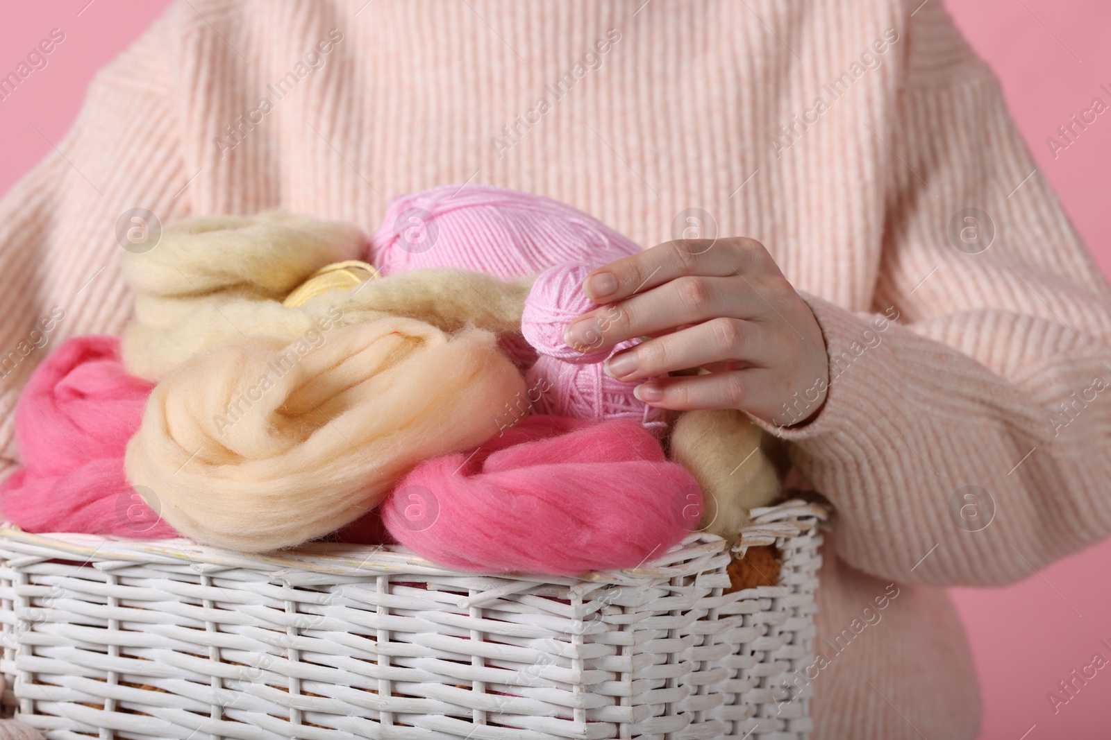 Photo of Woman holding wicker basket with colorful felting wool and yarns on pink background, closeup