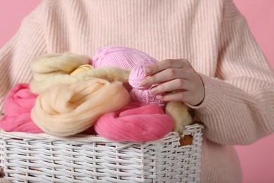 Photo of Woman holding wicker basket with colorful felting wool and yarns on pink background, closeup