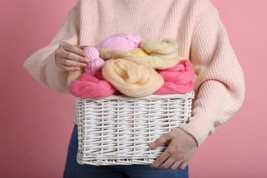 Photo of Woman holding wicker basket with colorful felting wool and yarns on pink background, closeup