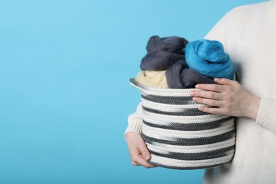 Photo of Woman holding wicker basket with colorful felting wool on light blue background, closeup. Space for text