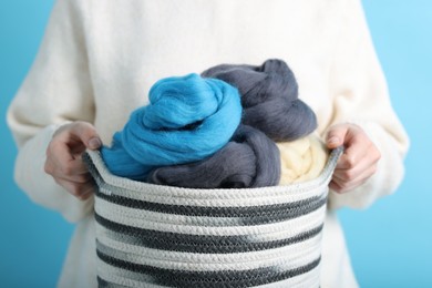 Photo of Woman holding wicker basket with colorful felting wool on light blue background, closeup