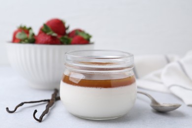 Photo of Tasty panna cotta with caramel, vanilla pods and strawberries on light table, closeup