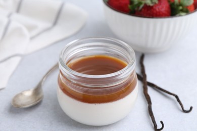 Photo of Tasty panna cotta with caramel, vanilla pods and strawberries on light table, closeup