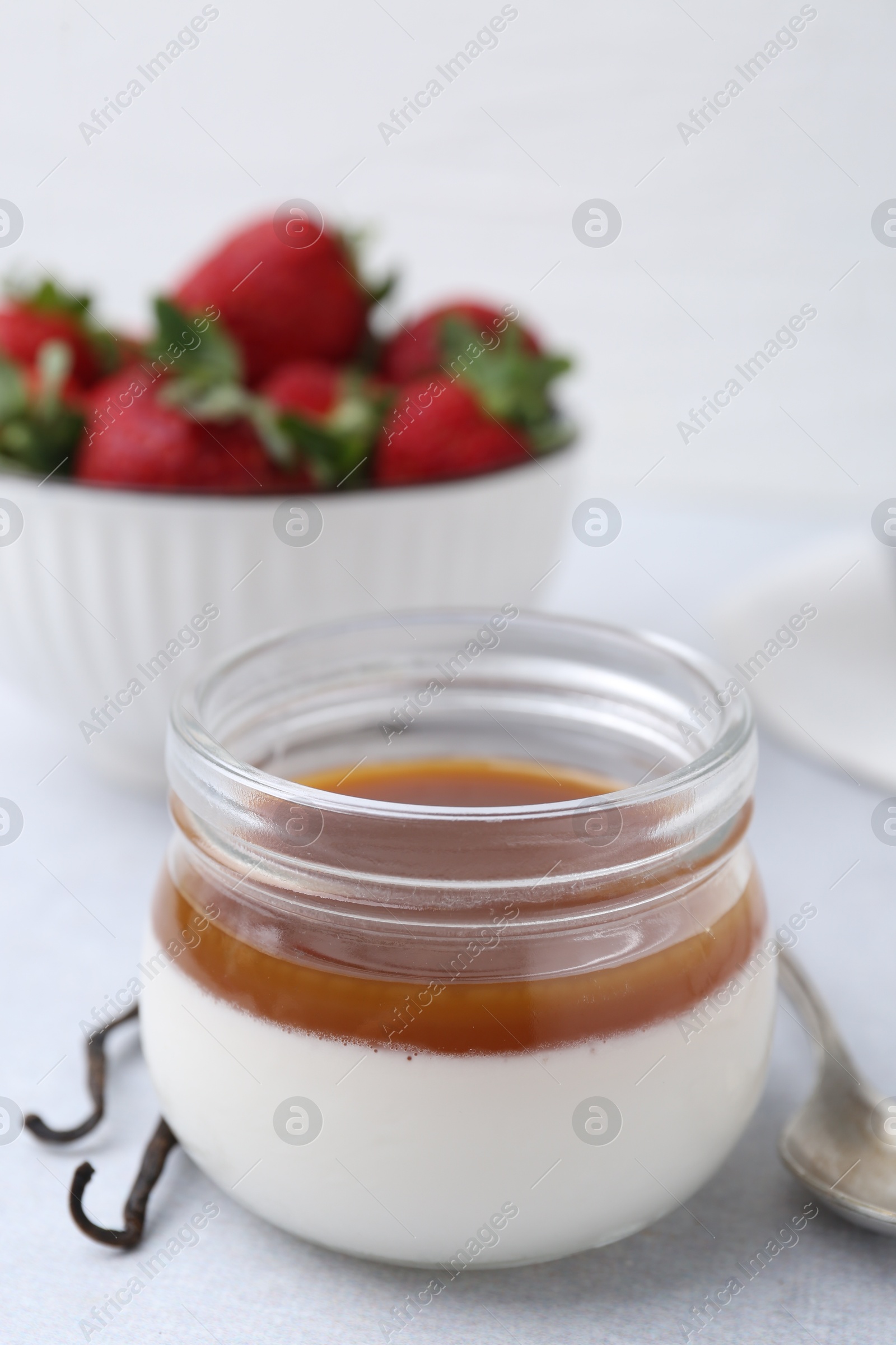 Tasty panna cotta with caramel, vanilla pods and strawberries on light table, closeup Photo of Tasty panna cotta with caramel, vanilla pods and strawberries on light table, closeup
