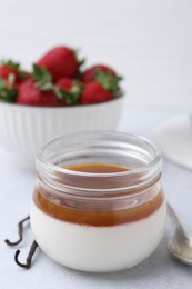 Photo of Tasty panna cotta with caramel, vanilla pods and strawberries on light table, closeup