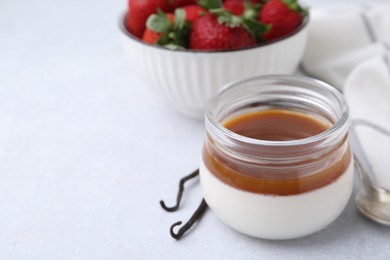 Photo of Tasty panna cotta with caramel, vanilla pods and strawberries on light table, closeup. Space for text