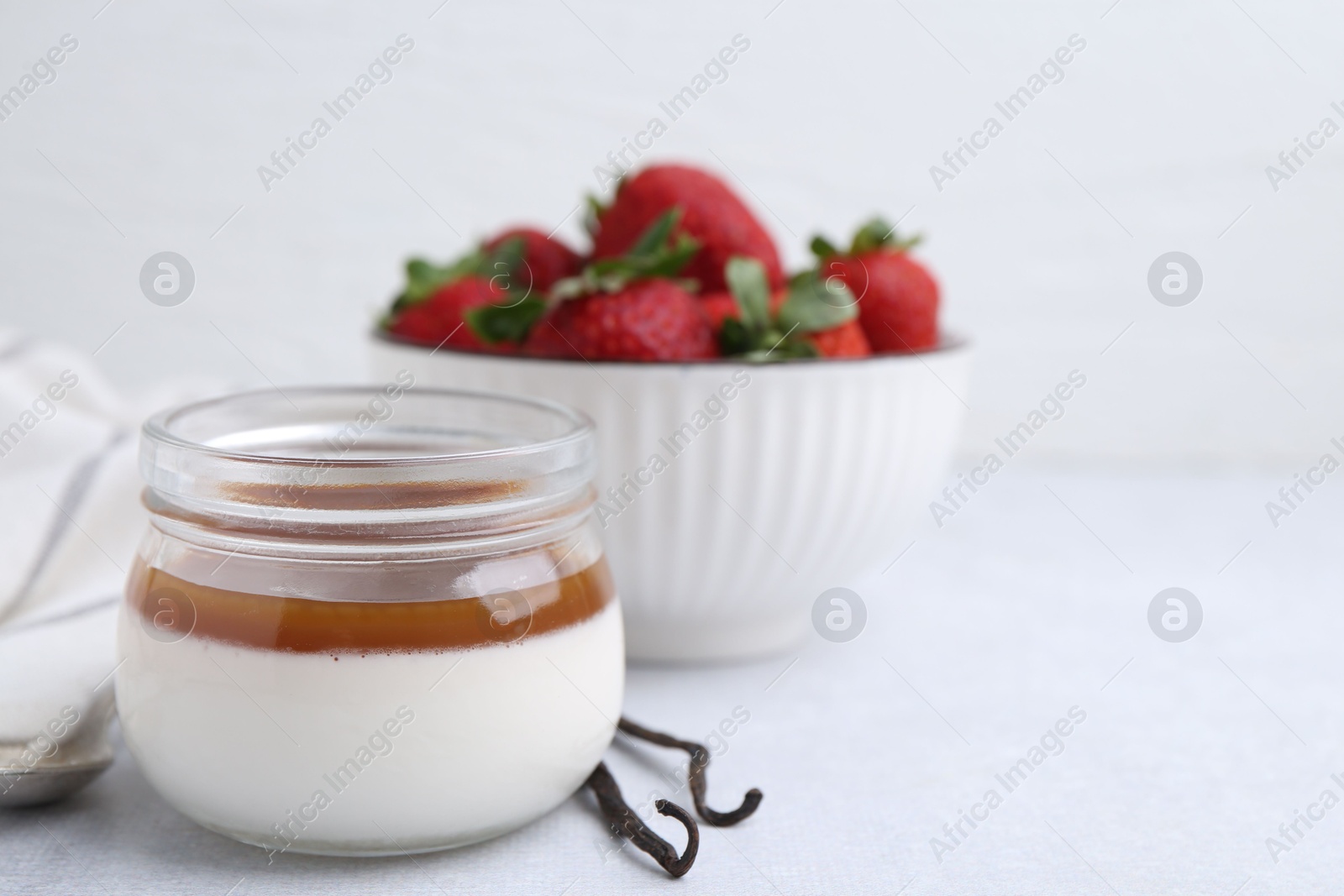Tasty panna cotta with caramel, vanilla pods and strawberries on light table, closeup. Space for text Photo of Tasty panna cotta with caramel, vanilla pods and strawberries on light table, closeup. Space for text