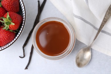 Photo of Tasty panna cotta with caramel, vanilla pods and strawberries on light table, flat lay