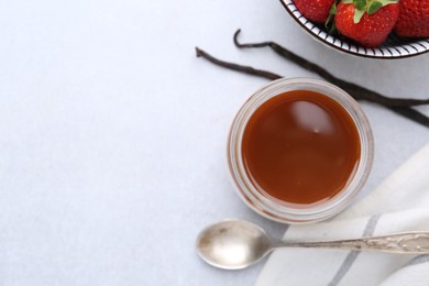 Photo of Tasty panna cotta with caramel, vanilla pods and strawberries on light table, flat lay. Space for text