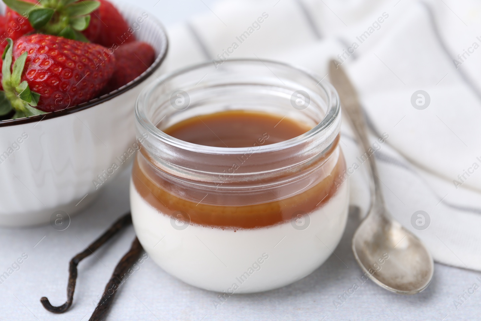 Tasty panna cotta with caramel, vanilla pods and strawberries on light table, closeup Photo of Tasty panna cotta with caramel, vanilla pods and strawberries on light table, closeup