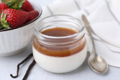 Photo of Tasty panna cotta with caramel, vanilla pods and strawberries on light table, closeup