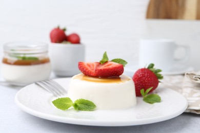 Photo of Tasty panna cotta with caramel, strawberries and mint on light table, closeup