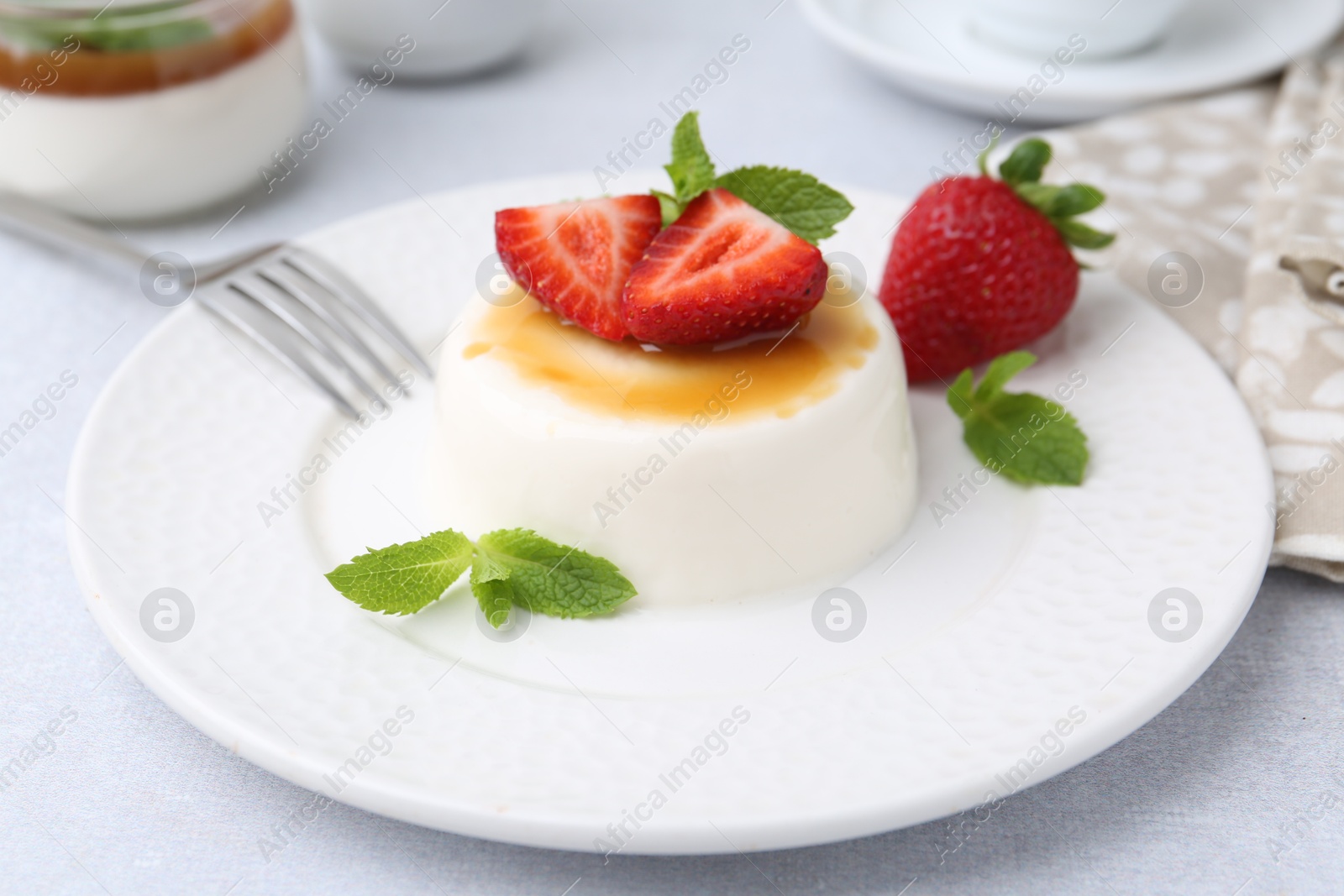 Tasty panna cotta with caramel, strawberries and mint on light table, closeup Photo of Tasty panna cotta with caramel, strawberries and mint on light table, closeup
