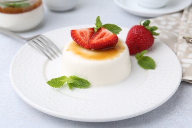 Photo of Tasty panna cotta with caramel, strawberries and mint on light table, closeup