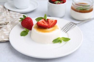 Photo of Tasty panna cotta with caramel, strawberries and mint on light table, closeup