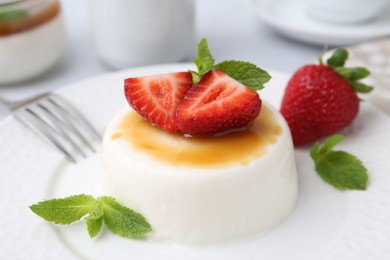 Photo of Tasty panna cotta with caramel, strawberries and mint on table, closeup