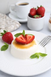 Photo of Tasty panna cotta with caramel, strawberries, mint and coffee on table, closeup