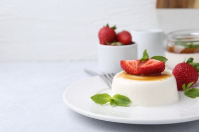 Photo of Tasty panna cotta with caramel, strawberries and mint on light table, closeup. Space for text