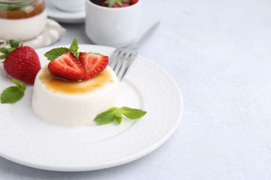 Photo of Tasty panna cotta with caramel, strawberries and mint on light table, closeup. Space for text
