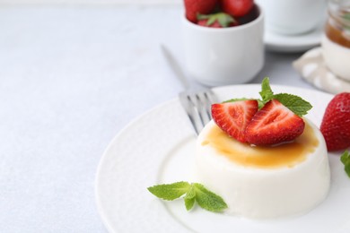 Photo of Tasty panna cotta with caramel, strawberries and mint on light table, closeup. Space for text
