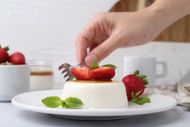 Photo of Woman eating tasty panna cotta at light table, closeup