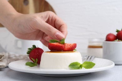Photo of Woman decorating tasty panna cotta with mint at light table, closeup