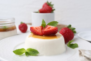 Photo of Tasty panna cotta with caramel, strawberries and mint on table, closeup