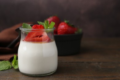 Photo of Tasty panna cotta with caramel, strawberries and mint on wooden table, closeup. Space for text