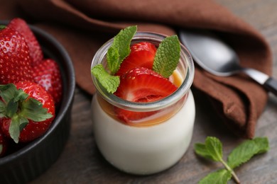 Photo of Tasty panna cotta with caramel, strawberries and mint on wooden table, closeup
