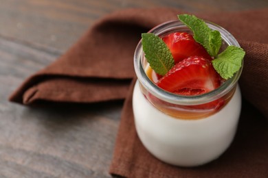 Photo of Tasty panna cotta with caramel, strawberries and mint on wooden table, closeup. Space for text