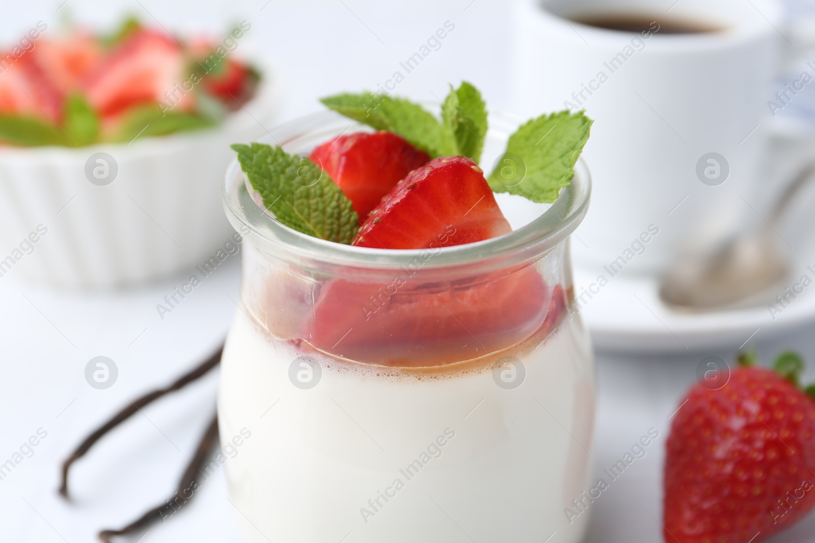 Tasty panna cotta with caramel, strawberries, mint, vanilla pods and coffee on white table, closeup Photo of Tasty panna cotta with caramel, strawberries, mint, vanilla pods and coffee on white table, closeup
