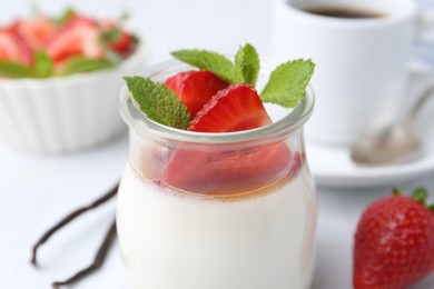 Photo of Tasty panna cotta with caramel, strawberries, mint, vanilla pods and coffee on white table, closeup
