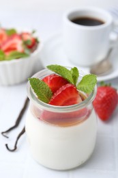 Photo of Tasty panna cotta with caramel, strawberries, mint, vanilla pods and coffee on white table, closeup