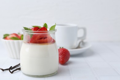 Photo of Tasty panna cotta with caramel, strawberries, mint, vanilla pods and coffee on white tiled table, closeup. Space for text