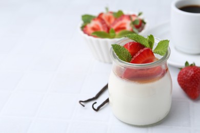 Photo of Tasty panna cotta with caramel, strawberries, mint, vanilla pods and coffee on white tiled table, closeup. Space for text