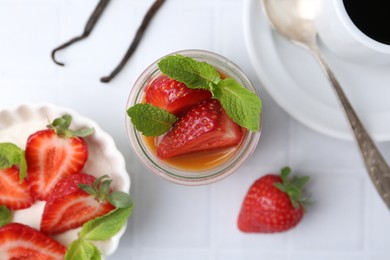 Photo of Tasty panna cotta with caramel, strawberries, mint, vanilla pods and coffee on white tiled table, flat lay