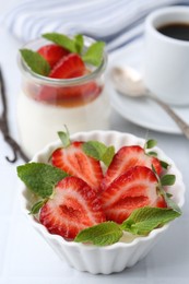 Photo of Tasty panna cotta with strawberries, mint, vanilla pods and coffee on white table, closeup