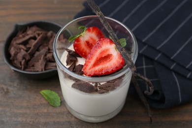 Photo of Tasty panna cotta with chocolate, strawberry, mint and vanilla pods on wooden table, closeup