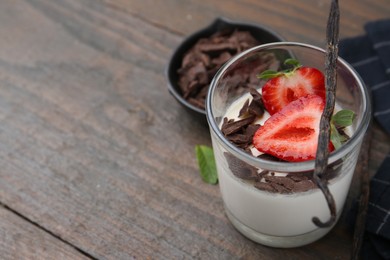 Photo of Tasty panna cotta with chocolate, strawberry, mint and vanilla pods on wooden table, closeup. Space for text