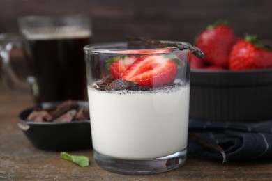 Photo of Tasty panna cotta with chocolate, strawberries, mint and vanilla pods on wooden table, closeup