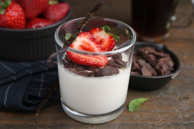Photo of Tasty panna cotta with chocolate, strawberries, mint and vanilla pods on wooden table, closeup