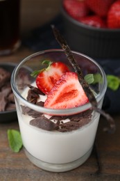 Photo of Tasty panna cotta with chocolate, strawberries, mint and vanilla pods on wooden table, closeup