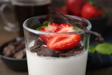 Photo of Tasty panna cotta with chocolate, strawberries, mint and vanilla pod on table, closeup