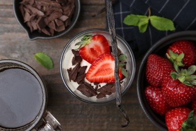 Photo of Tasty panna cotta with chocolate, strawberries, mint, vanilla pod and tea on wooden table, flat lay