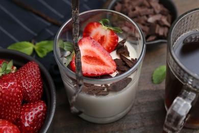 Photo of Tasty panna cotta with chocolate, strawberries, mint, vanilla pod and tea on wooden table, above view