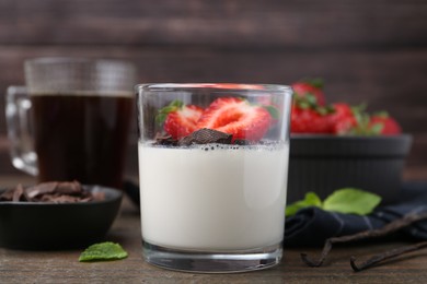 Photo of Tasty panna cotta with chocolate, strawberries, mint, vanilla pods and tea on wooden table, closeup