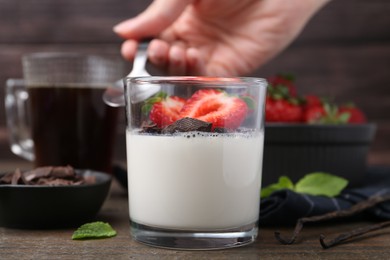 Photo of Woman eating tasty panna cotta at wooden table, closeup