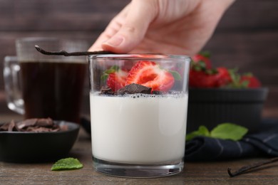 Photo of Woman decorating tasty panna cotta with vanilla pod at wooden table, closeup